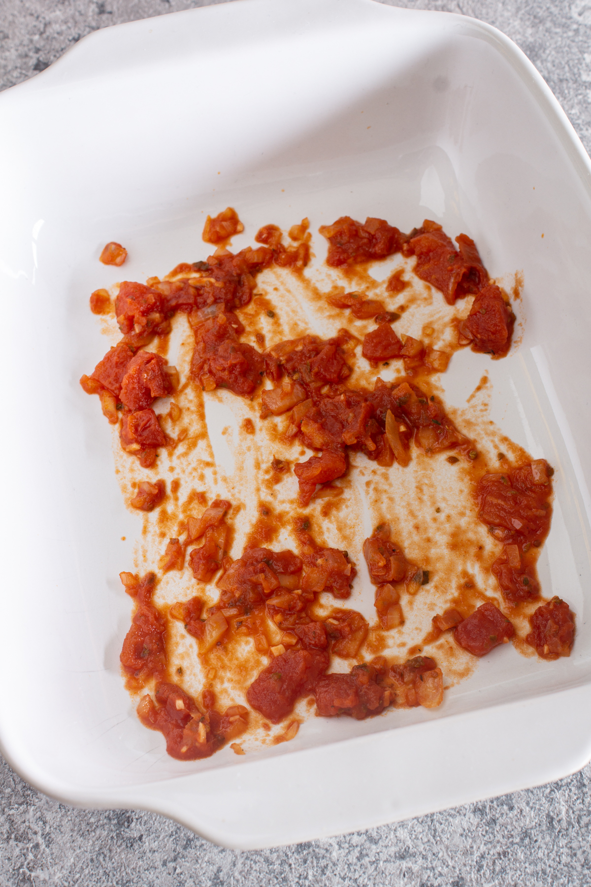 Die Auflaufform mit etwas Tomatensauce bestreichen