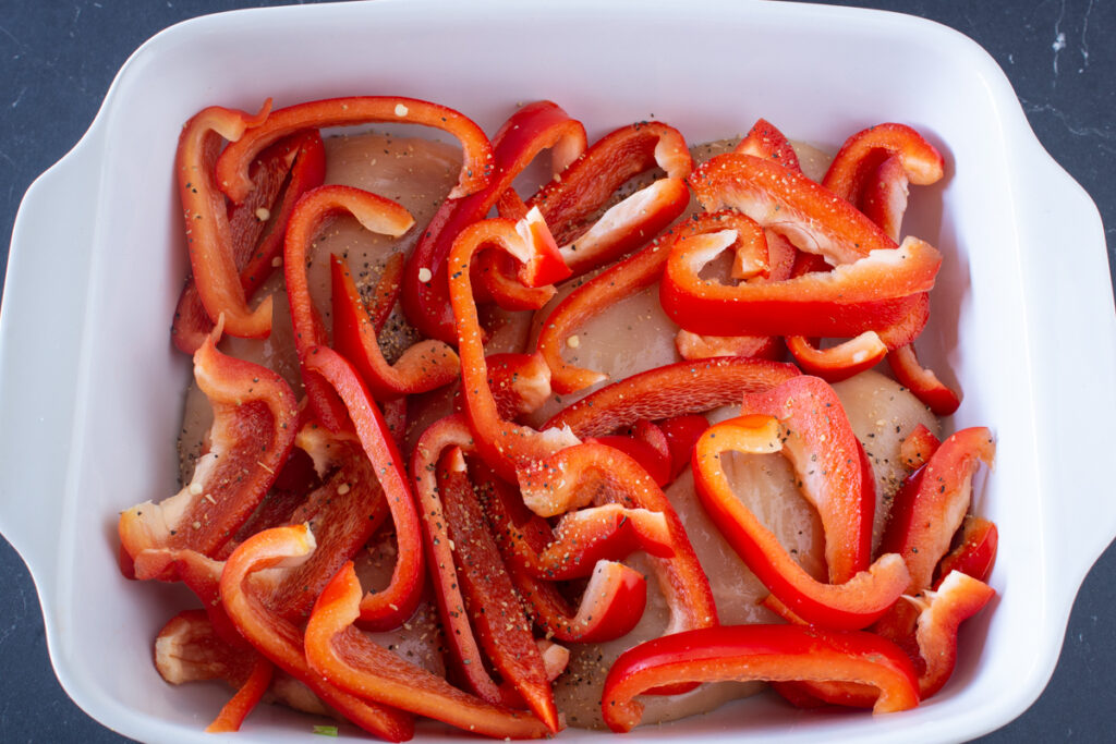 Hähnchenbrustfilets und Paprika in einer Auflaufform schichten